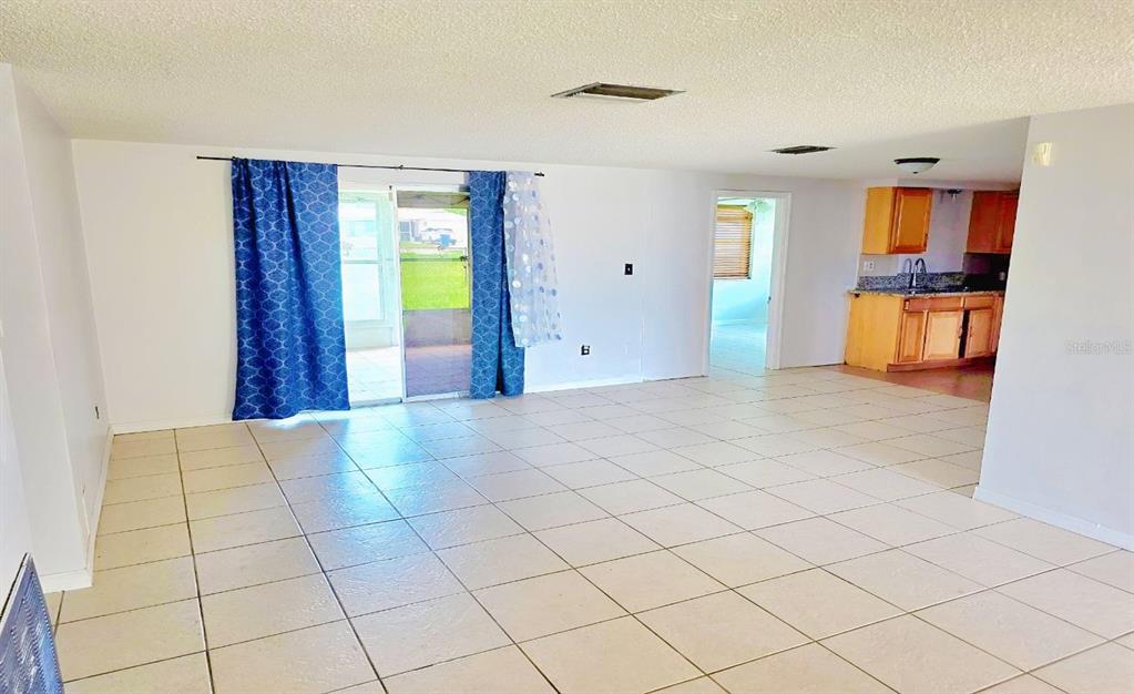 A spacious living room with light-colored tile flooring leads to a kitchen and sliding doors — 3806 BADEN DRIVE, HOLIDAY, FL