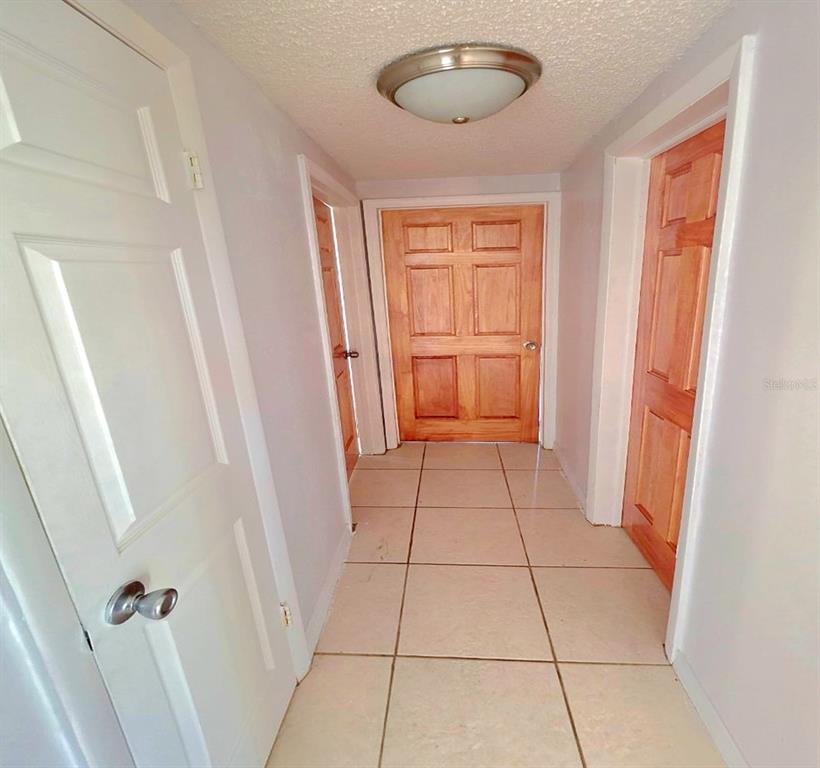 A hallway with light-colored tile flooring, white walls, and three wooden doors — 3806 BADEN DRIVE, HOLIDAY, FL