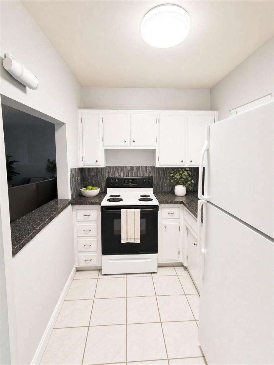 A galley kitchen features white cabinets, dark countertops, a black stove, and light tile flooring — 2409 NW 52nd Street, Tamarac FL 33309, TAMARAC, FL