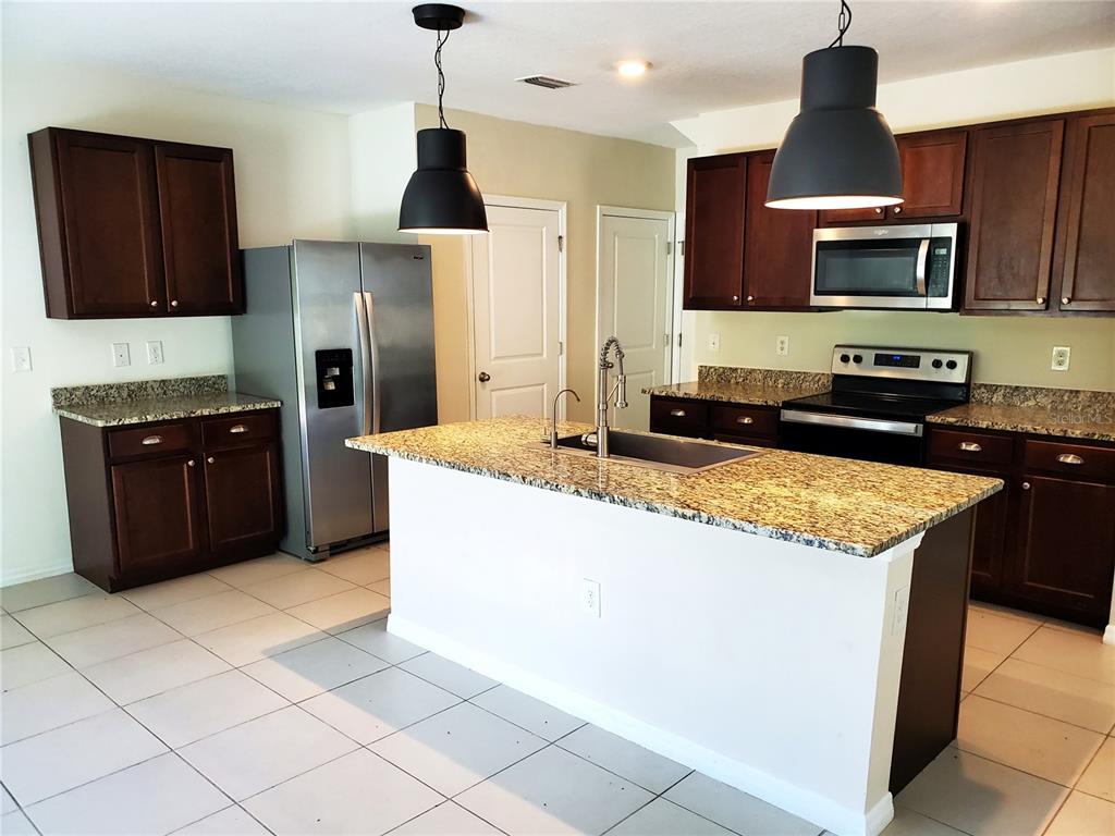 A kitchen features dark wood cabinets, granite countertops, stainless steel appliances, and a central island — 32871 BROOKS HAWK LANE, WESLEY CHAPEL, FL