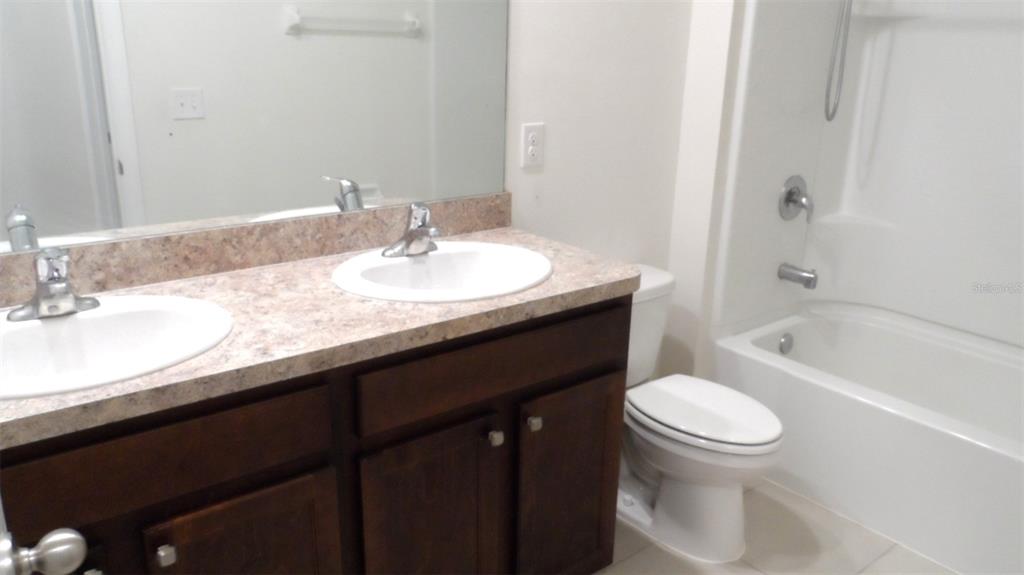 A bathroom features a double vanity with dark cabinets, a laminate countertop, and a shower-tub combo — 32871 BROOKS HAWK LANE, WESLEY CHAPEL, FL