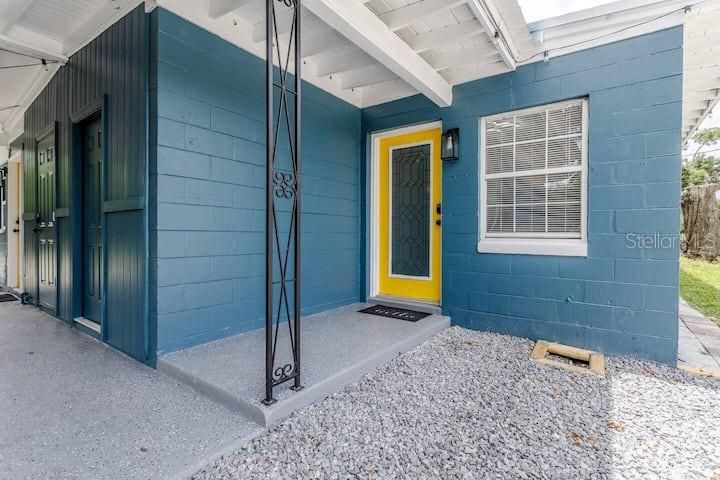 A blue concrete block house exterior features a bright yellow front door and gravel ground — 511 SAN JUAN BOULEVARD, ORLANDO, FL