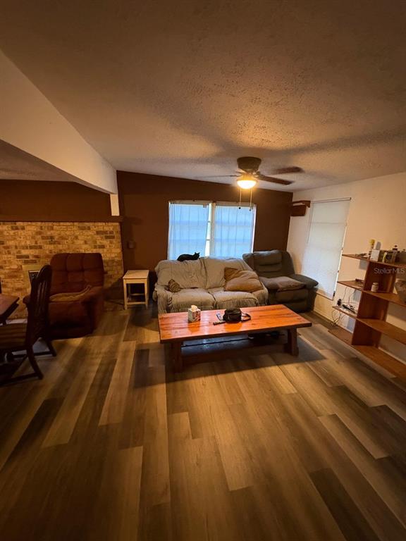 A living room features wood-look flooring, a brick fireplace, a ceiling fan, and wooden shelving — 18112 ALT STREET, SPRING HILL, FL