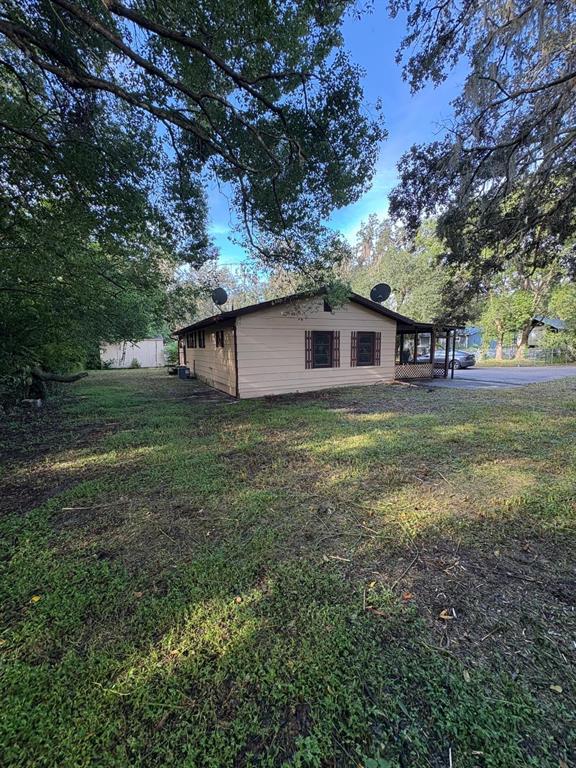 A tan, single-story house with a dark roof sits on a grassy lot with trees — 18112 ALT STREET, SPRING HILL, FL