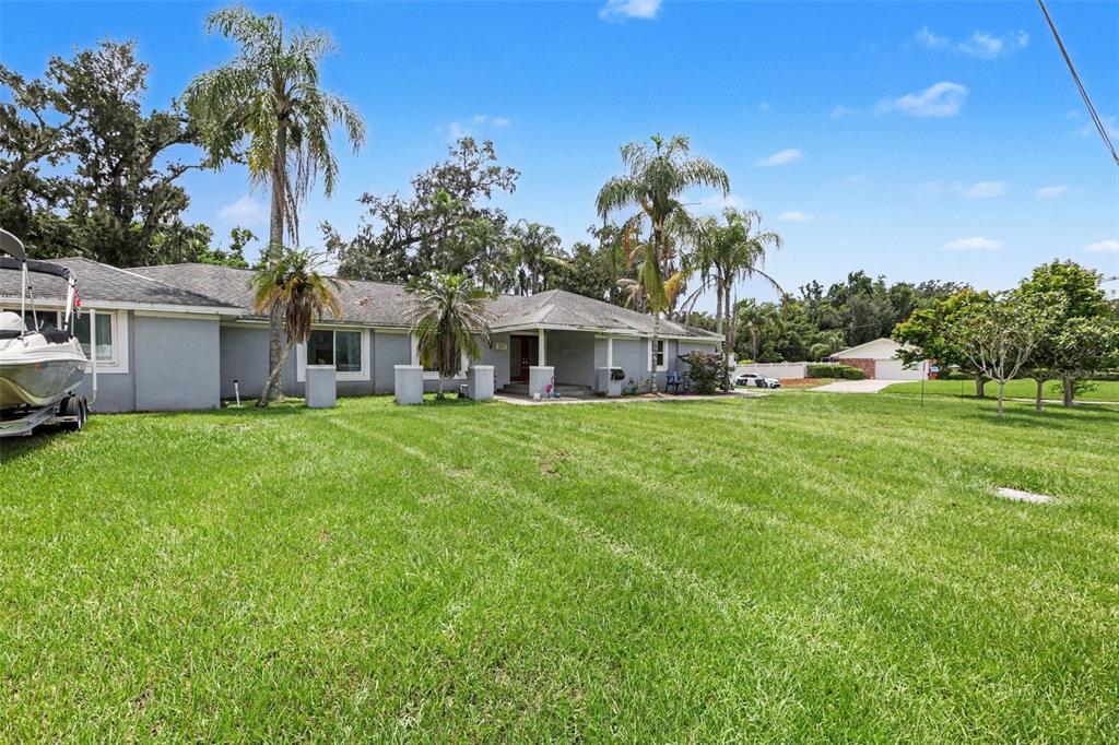 A single-story gray house with a large lawn, palm trees, and a boat on a trailer — 1307 BRANTWOOD DRIVE, VALRICO, FL