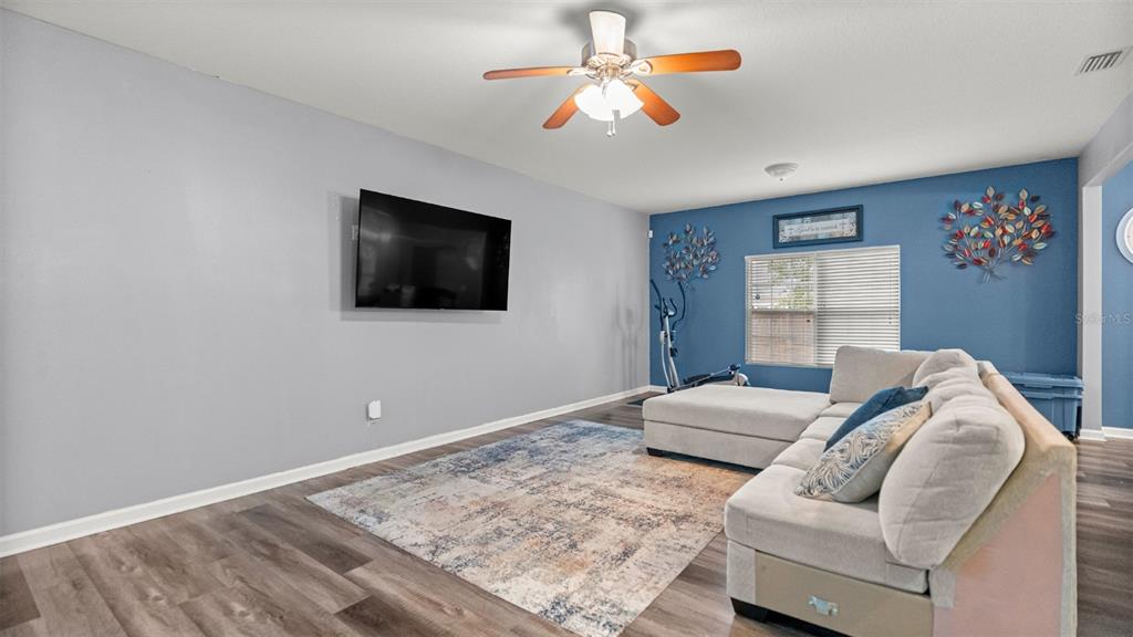 A living room features gray walls, a blue accent wall, wood-look flooring, and a sectional — 7745 NW 20TH WAY, GAINESVILLE, FL