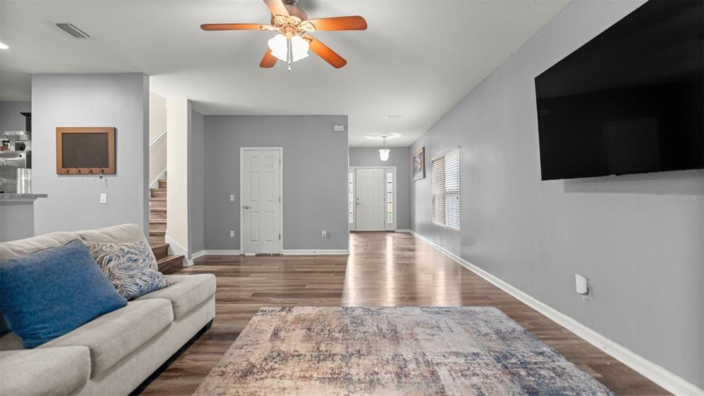 A living room features light gray walls, wood-look flooring, a ceiling fan, and a large television — 7745 NW 20TH WAY, GAINESVILLE, FL