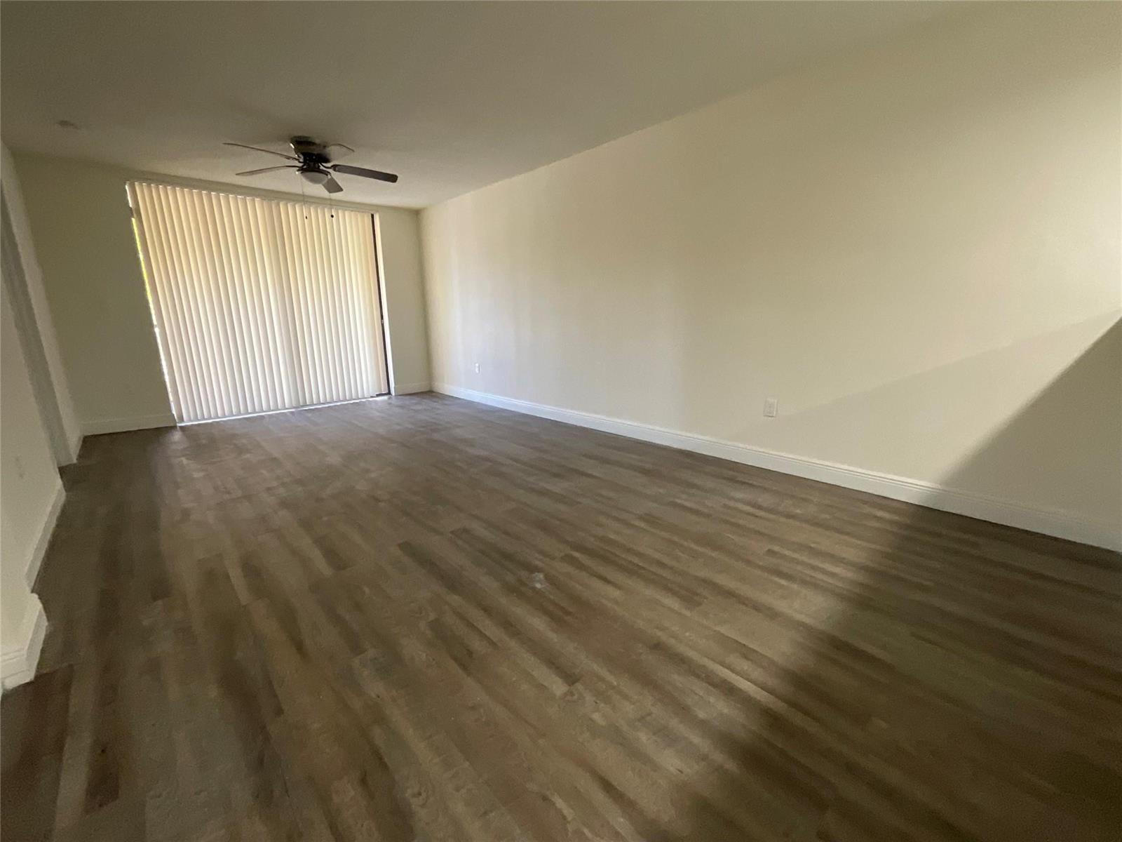 An empty living room features light-colored walls, wood-look flooring, and a ceiling fan — 18335 NW 68 Avenue # 104, Hialeah FL 33015, HIALEAH, FL