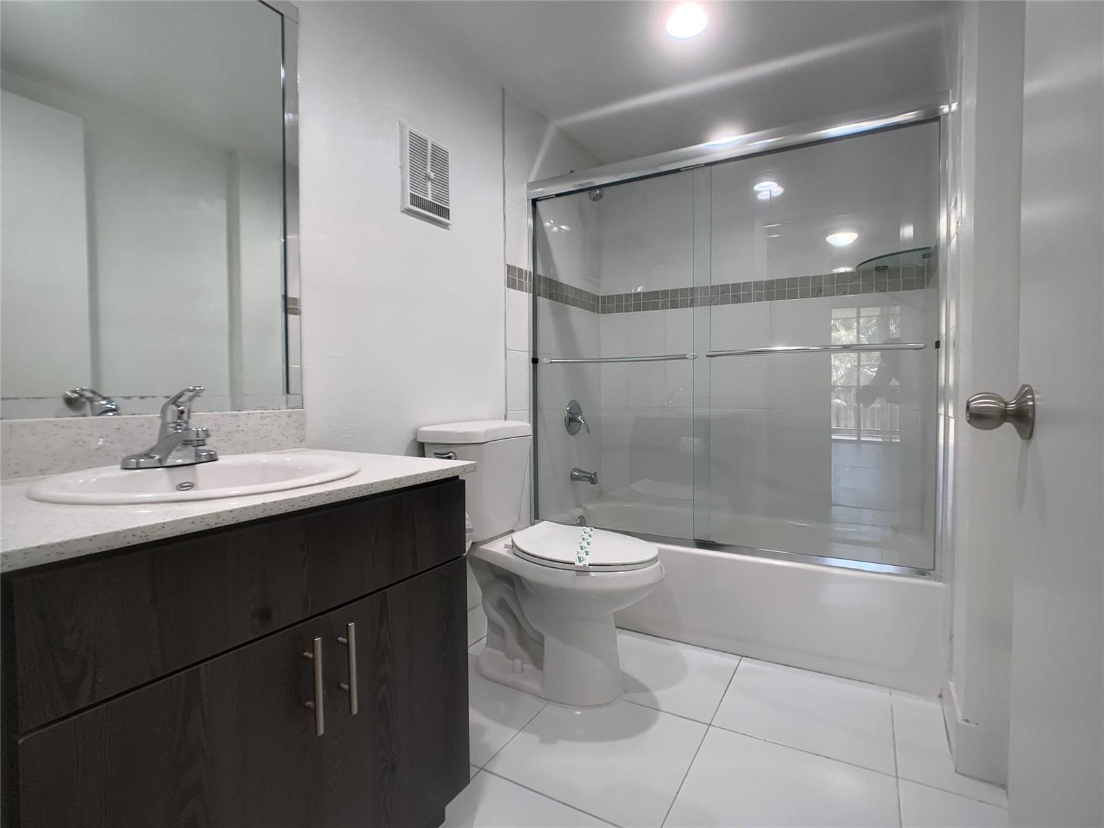A bathroom features a dark wood vanity, white countertop, toilet, and a glass-enclosed shower tub — 18335 NW 68 Avenue # 104, Hialeah FL 33015, HIALEAH, FL