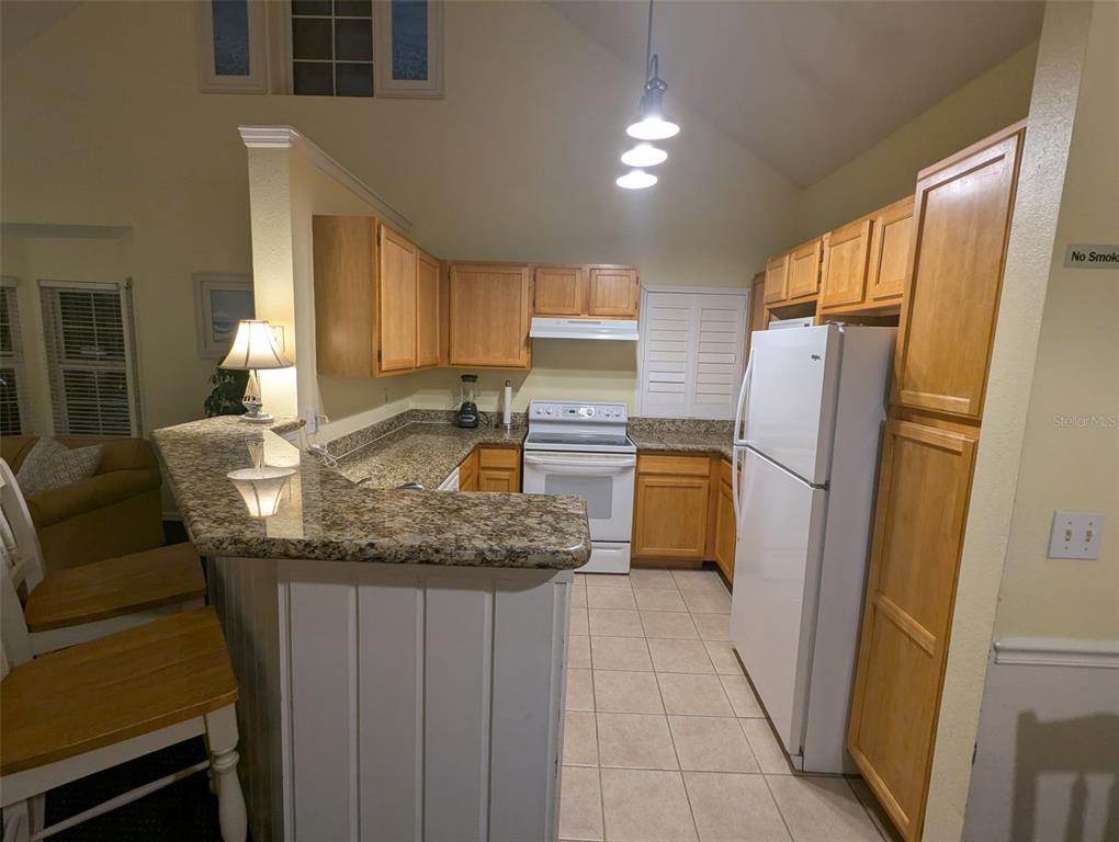 A kitchen features light wood cabinets, granite countertops, white appliances, and a breakfast bar — 3003 LIMBO LANE UNIT 203, KISSIMMEE, FL