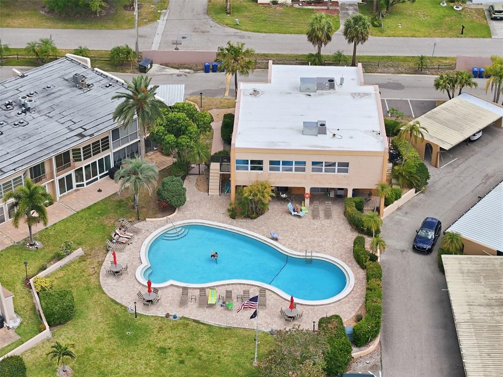 An aerial view shows a swimming pool surrounded by a patio, palm trees, and buildings — 225 COUNTRY CLUB DRIVE UNIT C332, LARGO, FL