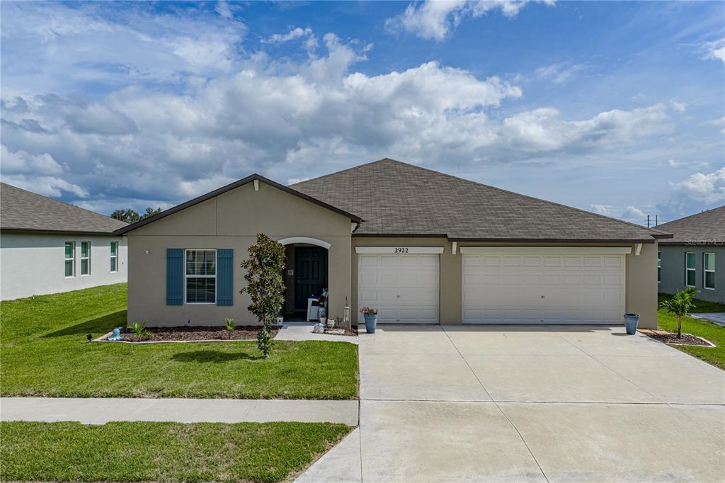 A single-story house with a beige stucco exterior, a three-car garage, and a lawn — 2922 FLYING BLACKBIRD ROAD, BARTOW, FL