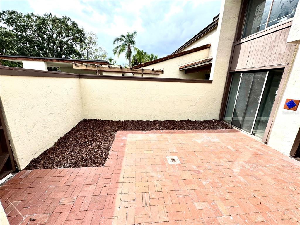 A brick patio sits beside a stucco wall and sliding glass doors in a courtyard — 4229 S LAKE ORLANDO PARKWAY UNIT 133, ORLANDO, FL