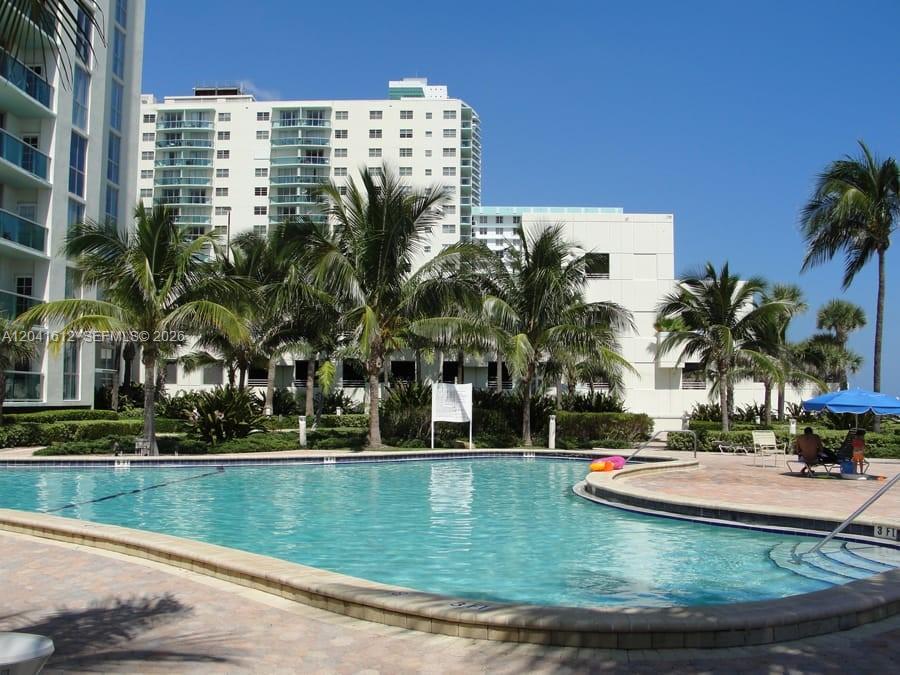 A swimming pool sits in front of a tall white apartment building with palm trees — 3901 S Ocean Dr # 8T, Hollywood FL 33019, HOLLYWOOD, FL