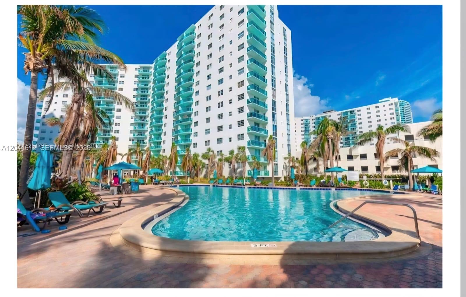 A large swimming pool sits in front of a tall white residential building with balconies — 3901 S Ocean Dr # 8T, Hollywood FL 33019, HOLLYWOOD, FL