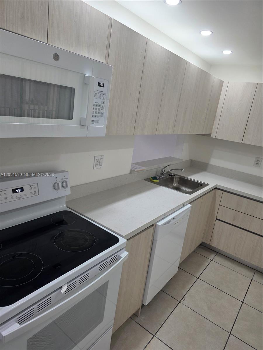 A kitchen features light wood cabinets, white appliances, a stainless steel sink, and tile flooring — 8025 SW 107th Ave # 202, Miami FL 33173, MIAMI, FL