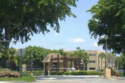 A gated entrance with a guardhouse and surrounding trees leads to a multi-story apartment building — 8025 SW 107th Ave # 202, Miami FL 33173, MIAMI, FL