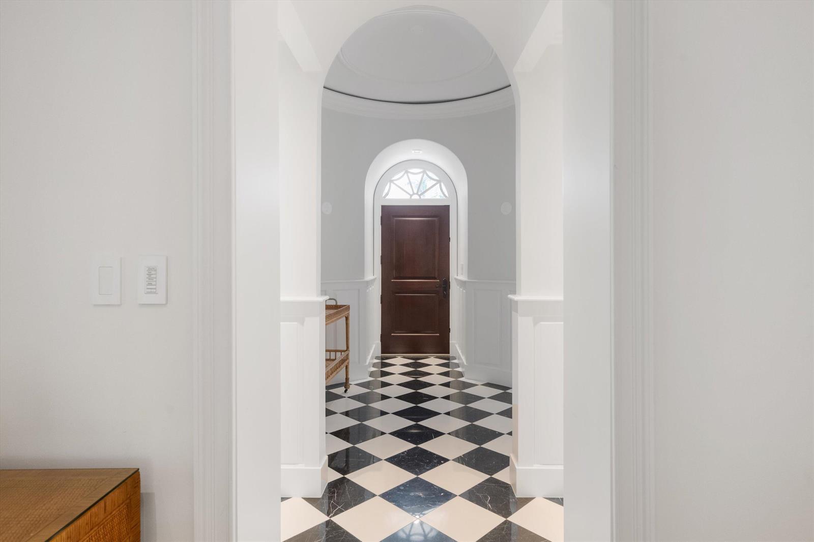 A hallway with a black and white checkered floor leads to a dark wood front door — 750 S County Road, Palm Beach FL 33480, PALM BEACH, FL