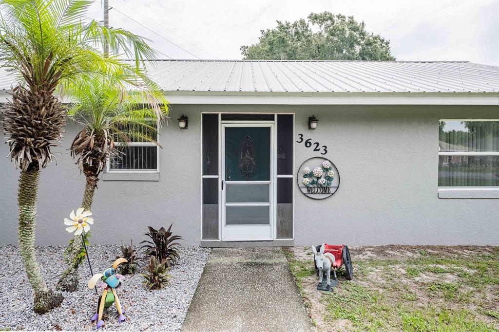 The exterior of a gray house features a metal roof, a front door, and landscaping — 3623 OPAL DRIVE, MULBERRY, FL