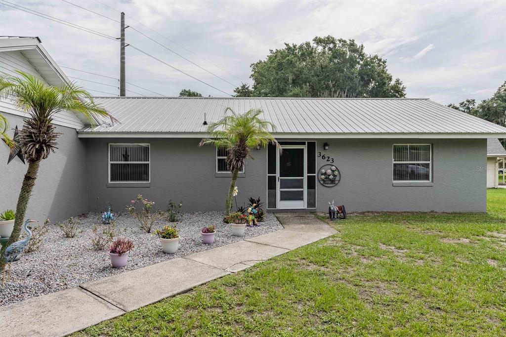 A gray, single-story house with a metal roof, a concrete walkway, and a landscaped yard — 3623 OPAL DRIVE, MULBERRY, FL
