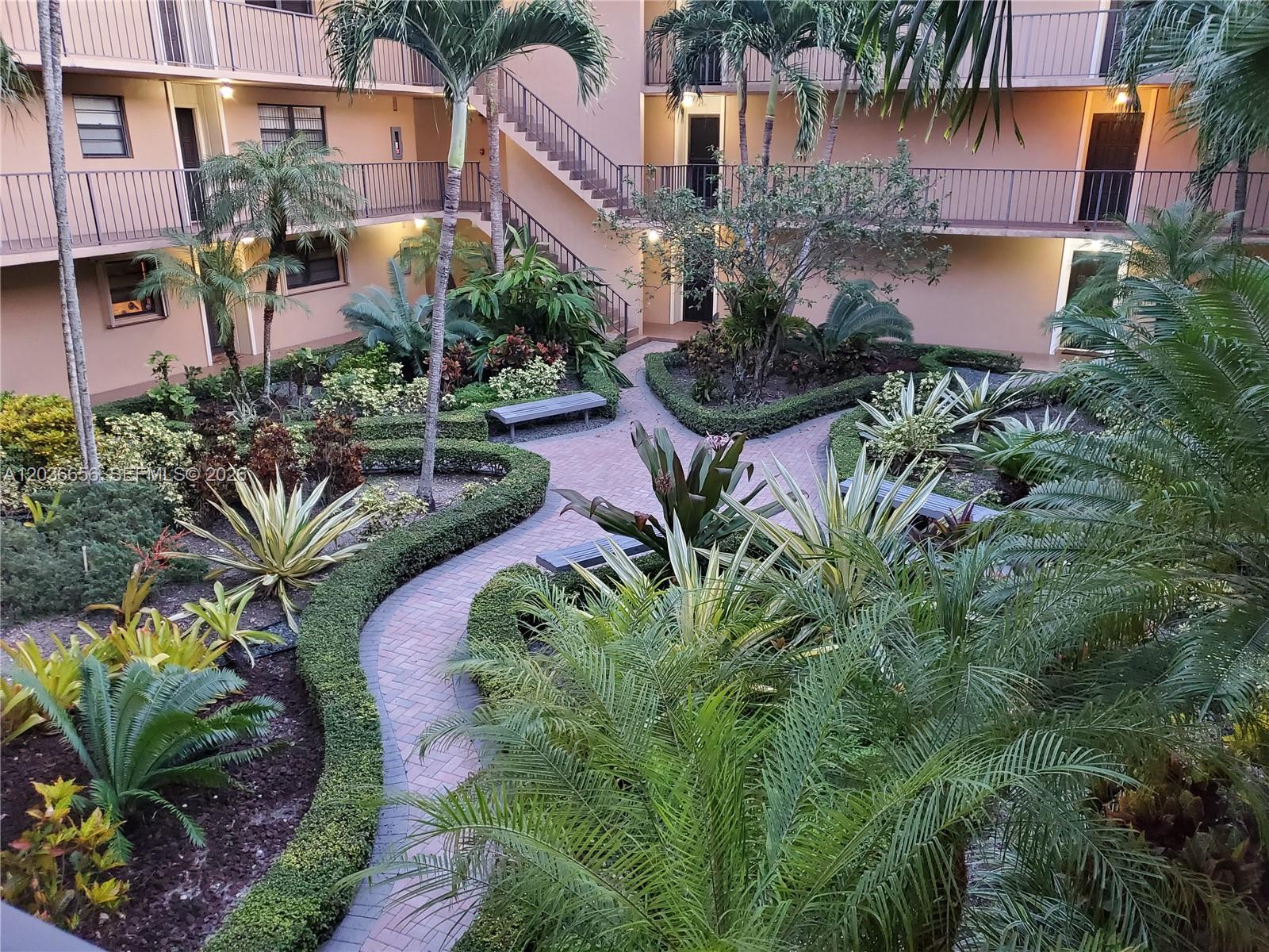 An elevated view of a landscaped courtyard with brick walkways, palm trees, and apartment balconies — 10425 SW 112th Ave # 207, Miami FL 33176, MIAMI, FL