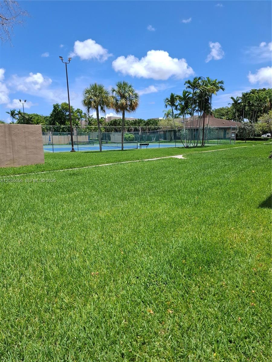 A grassy lawn leads to a fenced tennis court with palm trees under a blue sky — 10425 SW 112th Ave # 207, Miami FL 33176, MIAMI, FL