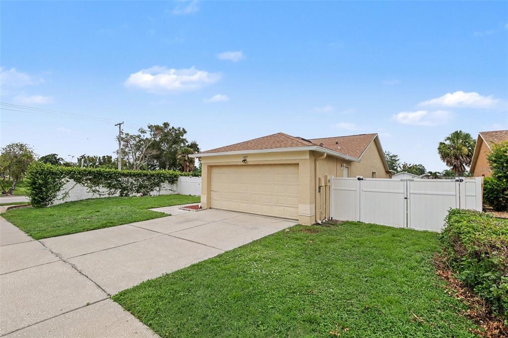 A beige house exterior features a two-car garage, a concrete driveway, and white vinyl fencing — 1607 WIDELAKE COURT, BRANDON, FL