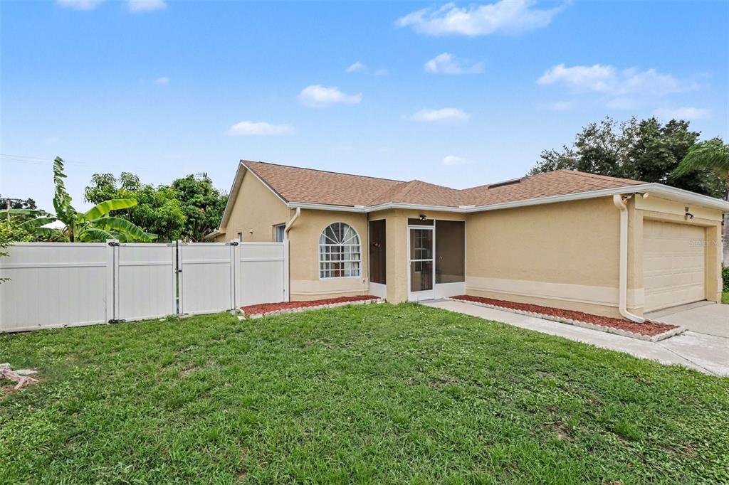 A single-story house with a tan stucco exterior, a brown shingled roof, and a white fence — 1607 WIDELAKE COURT, BRANDON, FL