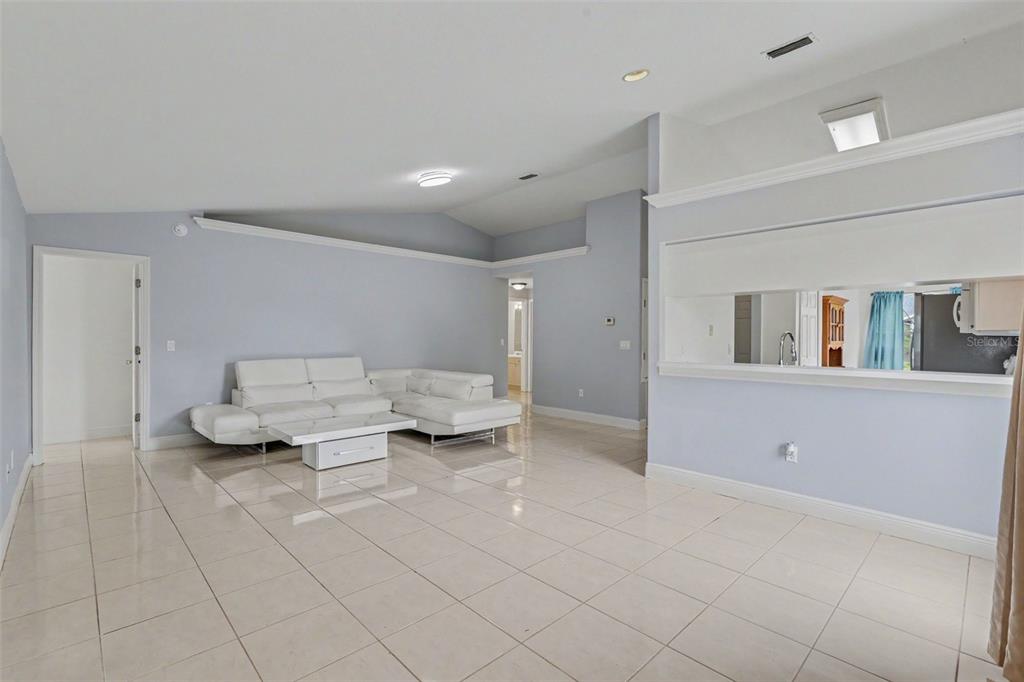 A living room with light-colored tile flooring, a white sectional sofa, and a kitchen pass-through — 1607 WIDELAKE COURT, BRANDON, FL