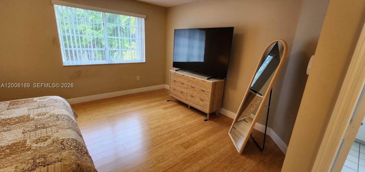 A bedroom features light wood flooring, a dresser with a television, and a floor mirror — 9309 SW 166th Ct, Miami FL 33196, MIAMI, FL