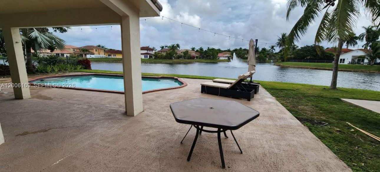 A covered patio overlooks a swimming pool and a lake with a fountain — 9309 SW 166th Ct, Miami FL 33196, MIAMI, FL