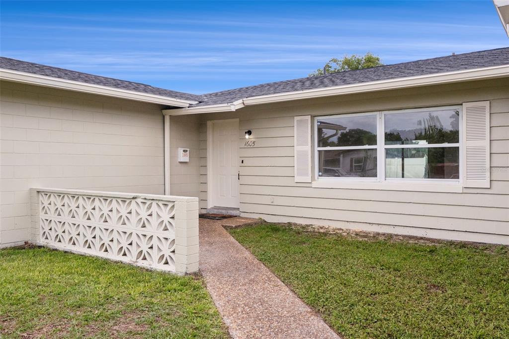 The exterior of a single-story house features light-colored siding, a concrete walkway, and a decorative screen — 1605 PURITAN AVENUE, WINTER PARK, FL