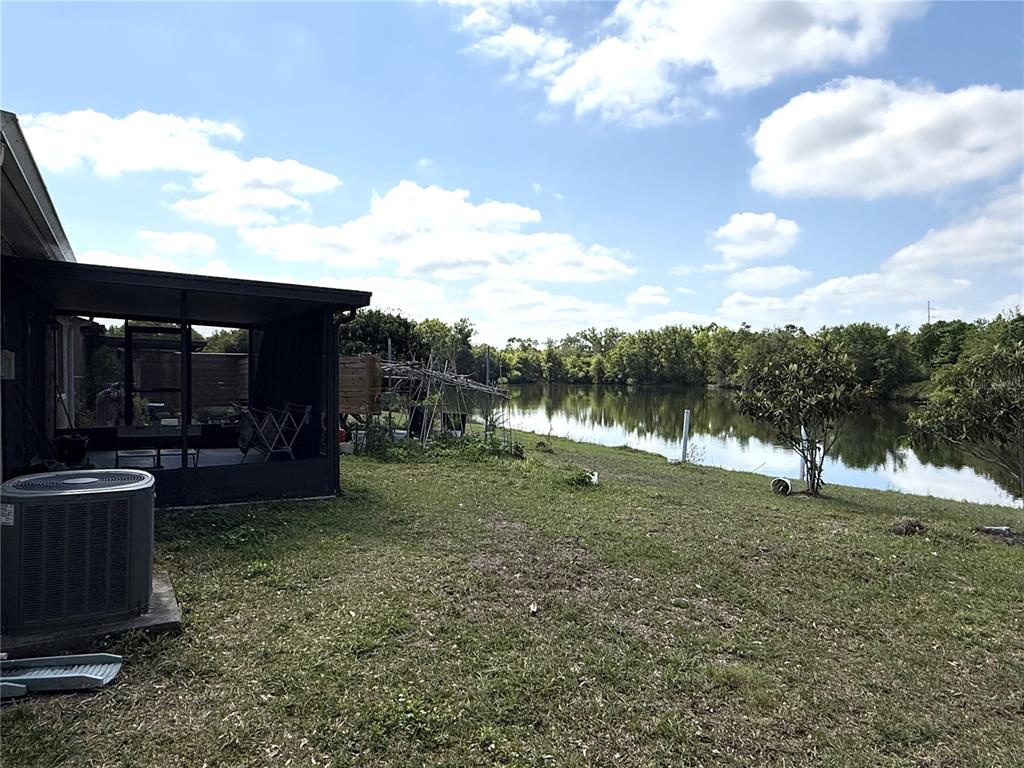 A backyard view featuring a screened-in patio, an air conditioning unit, and a pond — 14022 CITRUS POINTE DRIVE, TAMPA, FL