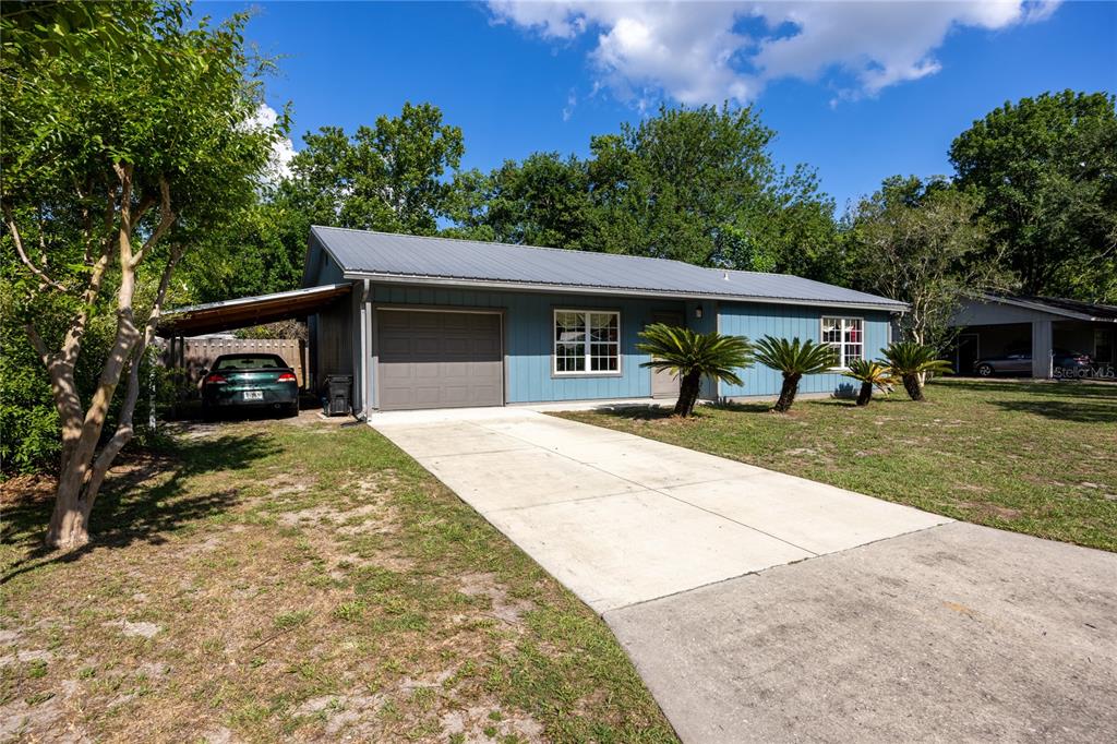 A blue single-story house with a metal roof, attached carport, and concrete driveway — 6517 NW 27TH STREET, GAINESVILLE, FL