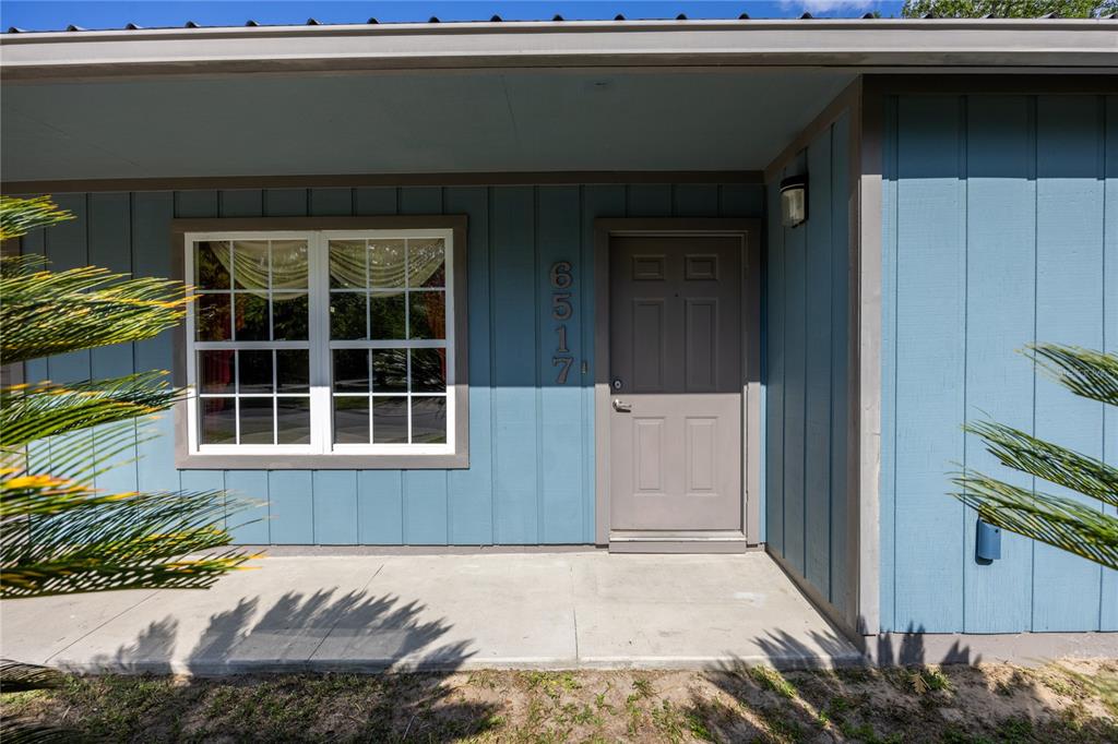 The exterior of a blue house features a concrete porch, a window, and a door — 6517 NW 27TH STREET, GAINESVILLE, FL
