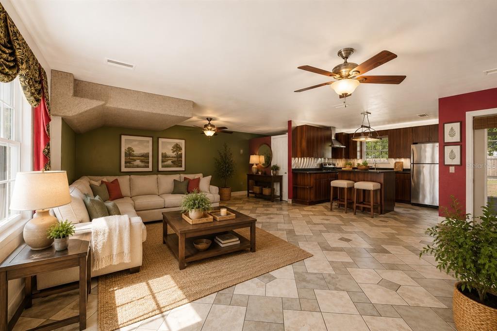 An open-concept living room and kitchen featuring tile flooring, a sectional sofa, and wood cabinetry — 6517 NW 27TH STREET, GAINESVILLE, FL