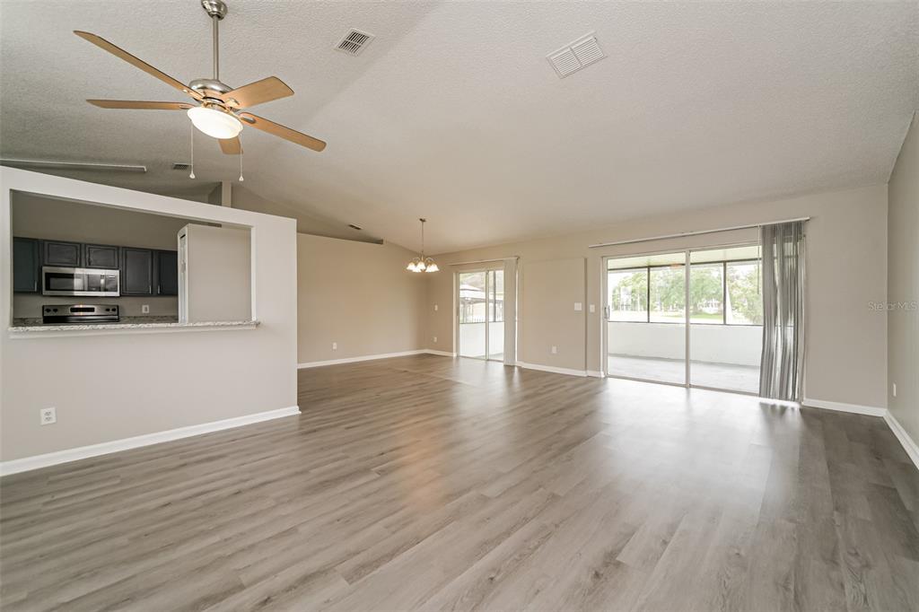 An open-concept living area with light wood-look flooring, a ceiling fan, and sliding glass doors — 602 COTULLA DRIVE, KISSIMMEE, FL