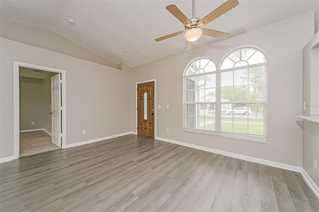 An empty room with gray wood-look flooring, a ceiling fan, and a front entrance door — 602 COTULLA DRIVE, KISSIMMEE, FL