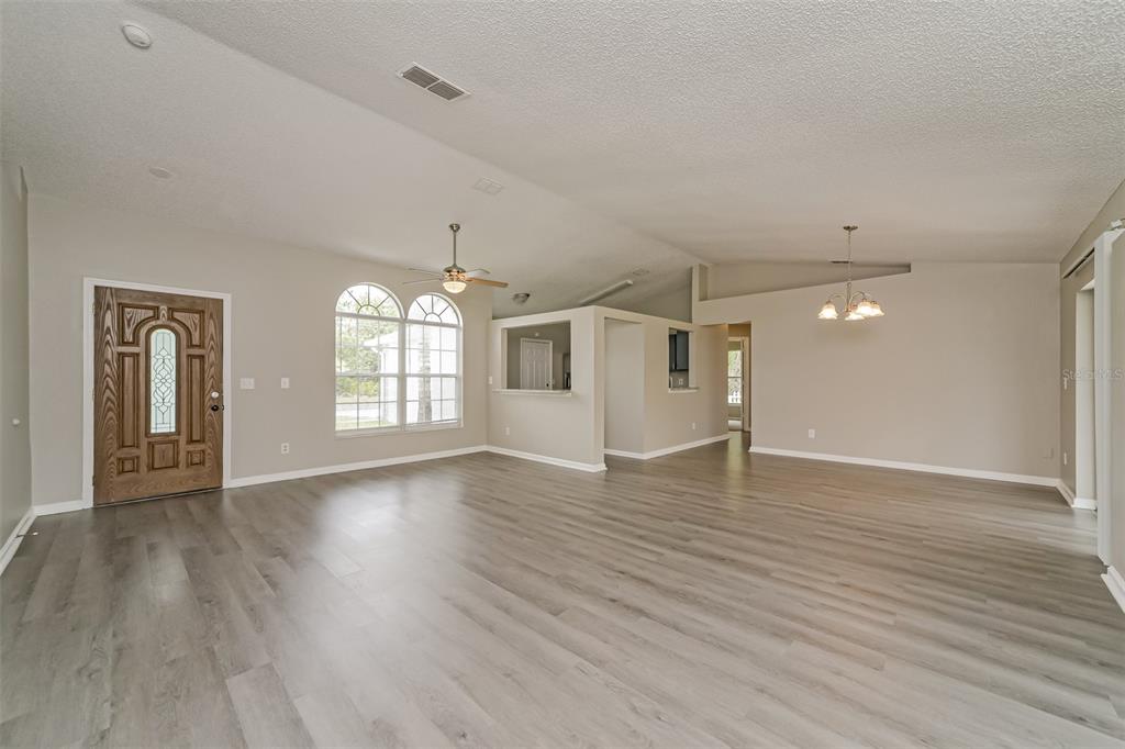 An open-concept living and dining area features light gray wood-look flooring and vaulted ceilings — 602 COTULLA DRIVE, KISSIMMEE, FL