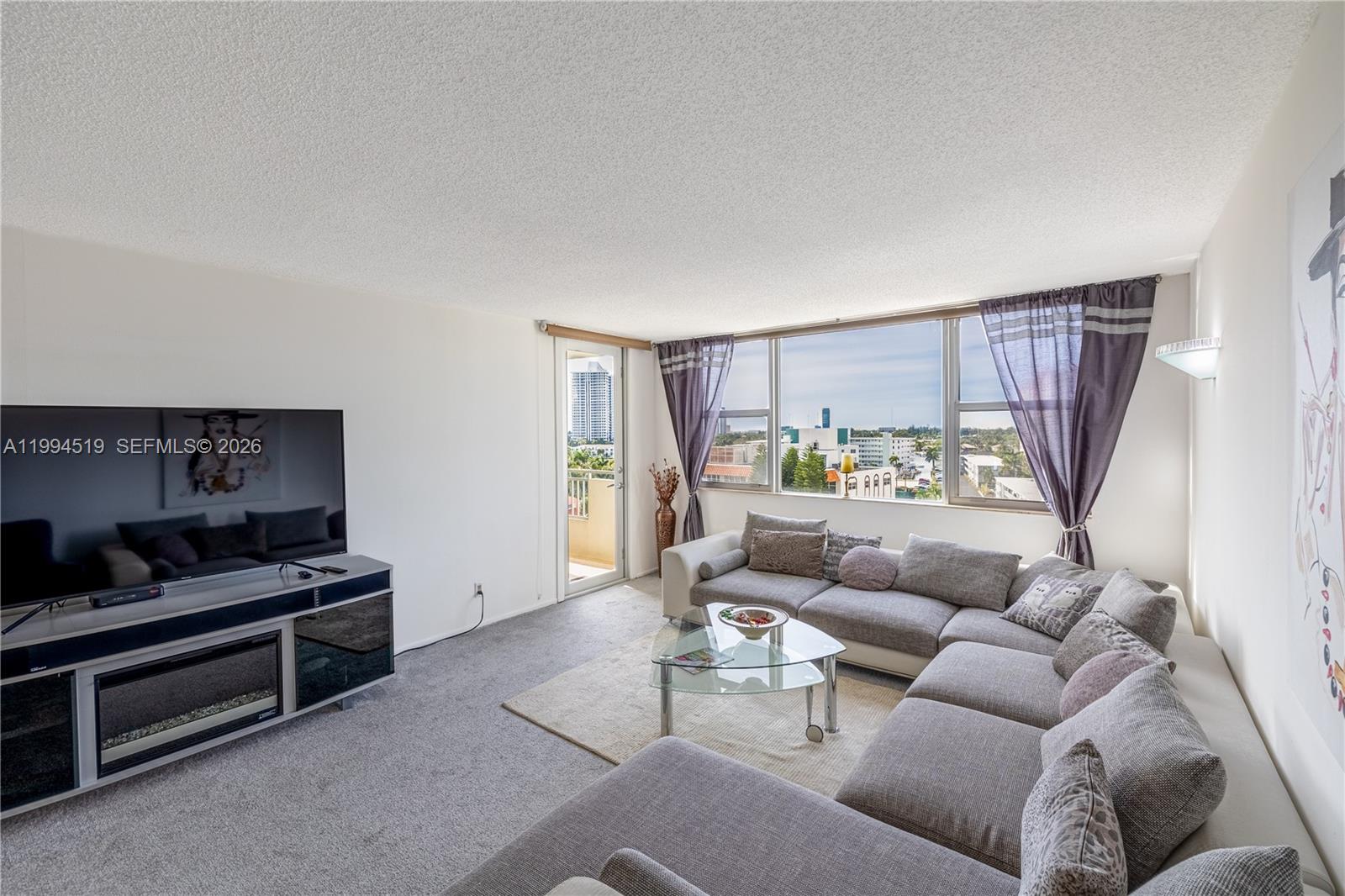 A living room features a large sectional sofa, a television console, and a balcony door — 3180 S Ocean Dr # 718, Hallandale Beach FL 33009, HALLANDALE BEACH, FL