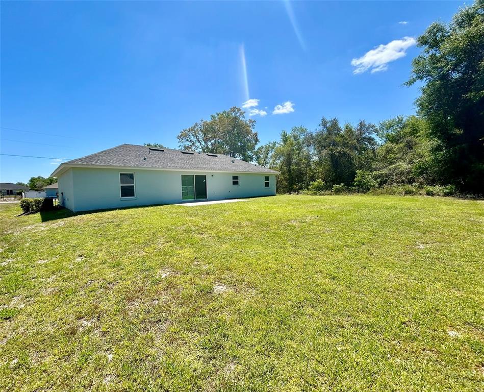 The rear exterior of a light-colored house features a sliding glass door and a large yard — 13300 SW 43RD COURT, OCALA, FL