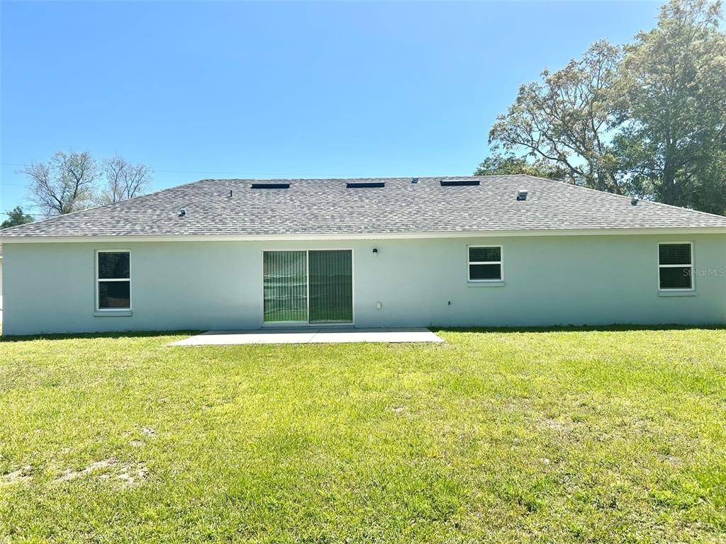 The rear exterior of a single-story house features a light-colored facade, sliding glass doors, and windows — 13300 SW 43RD COURT, OCALA, FL