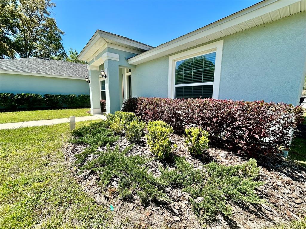 A light blue house exterior features a front entrance, a window, and landscaped garden beds — 13300 SW 43RD COURT, OCALA, FL