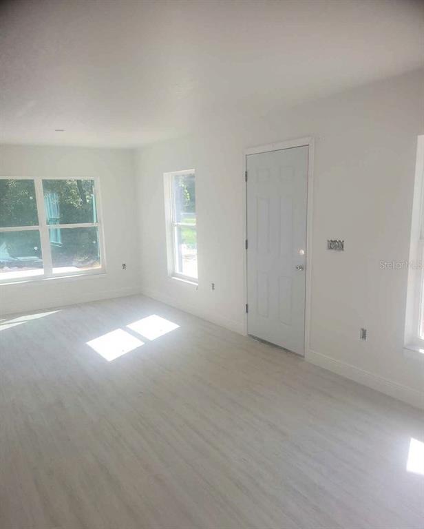 A bright, empty room features light-colored wood-look flooring, white walls, and several windows — 79 NE 156TH COURT, WILLISTON, FL
