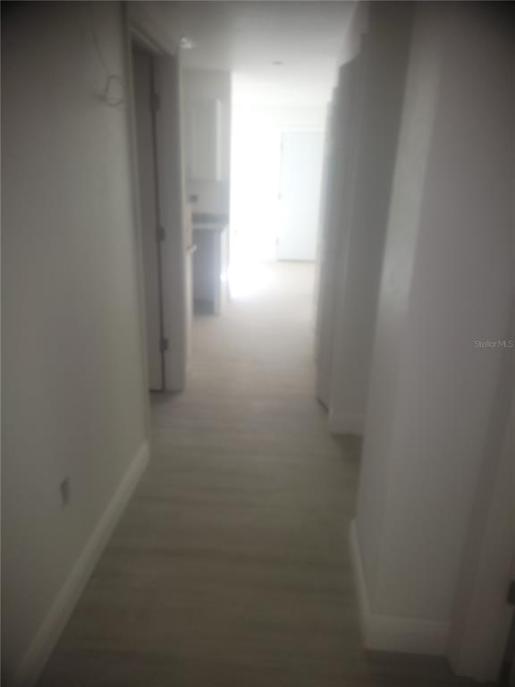 A hallway with light-colored flooring leads toward a bright doorway in the distance — 79 NE 156TH COURT, WILLISTON, FL