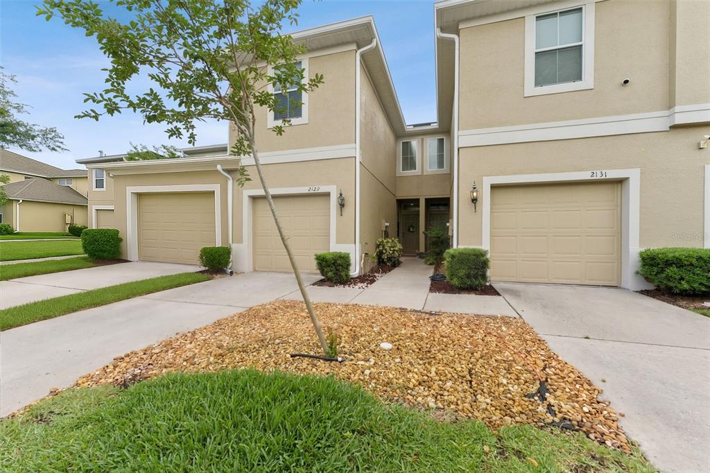 A two-story townhouse exterior features tan stucco walls, beige garage doors, and a gravel bed — 2129 LENNOX DALE LANE, BRANDON, FL