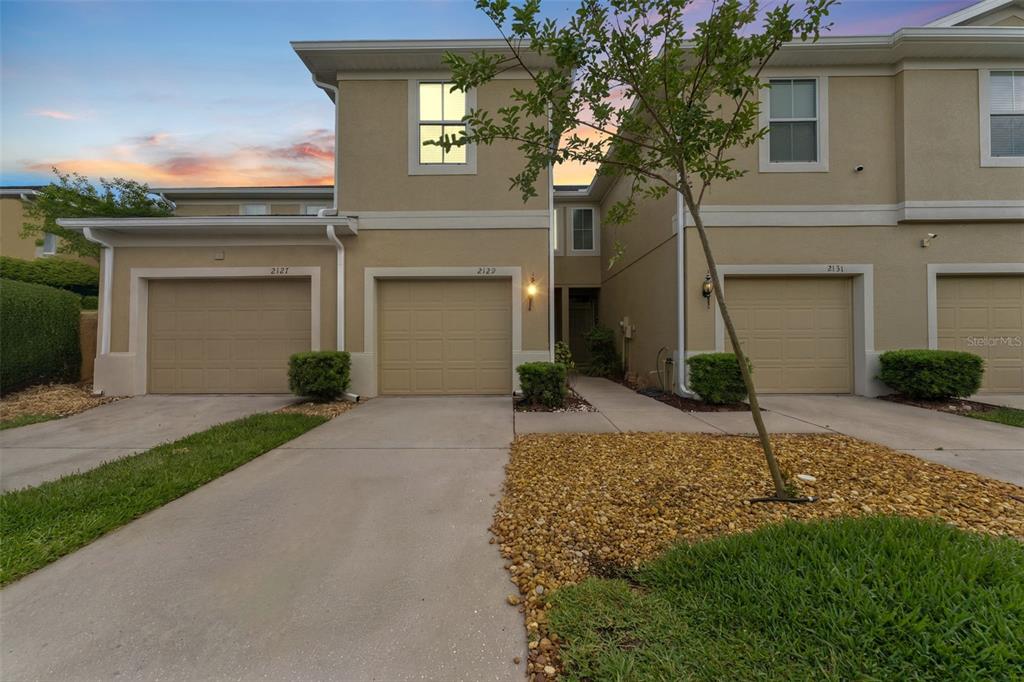 The exterior of a two-story townhouse complex features beige stucco walls and three garage doors — 2129 LENNOX DALE LANE, BRANDON, FL
