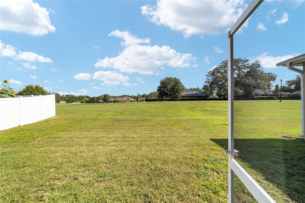 A view from a screened-in patio looking out over a large, open grassy backyard — 4417 SW 65TH PLACE, OCALA, FL