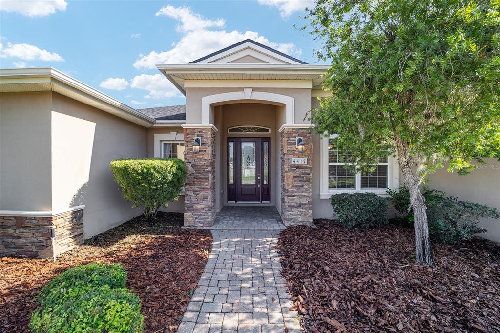 A stone-accented entryway leads to a dark front door on a beige stucco house — 4417 SW 65TH PLACE, OCALA, FL