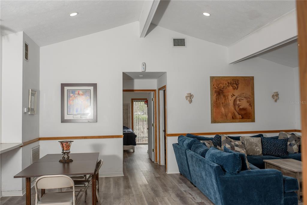 A living and dining area features vaulted ceilings, wood-look flooring, and a blue sectional sofa — 5644 ANTOINETTE STREET, SARASOTA, FL